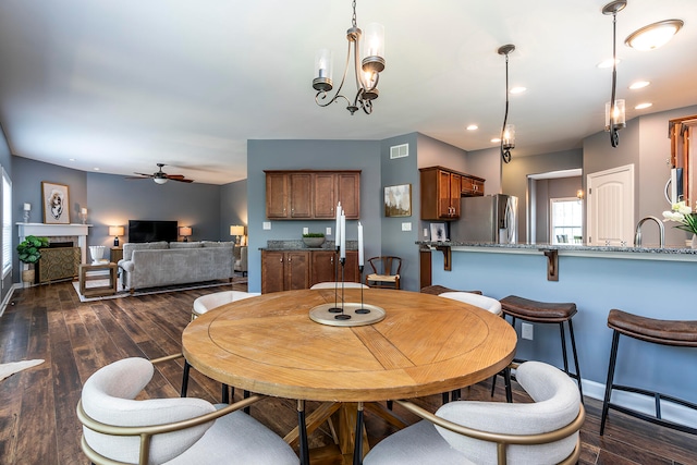 dining room with ceiling fan with notable chandelier, sink, and dark wood-type flooring