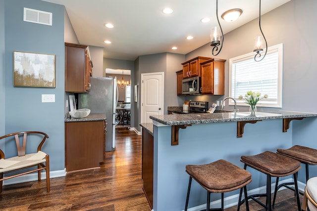 kitchen with appliances with stainless steel finishes, a kitchen breakfast bar, decorative light fixtures, dark hardwood / wood-style floors, and a notable chandelier