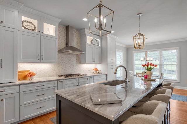 kitchen with crown molding, wall chimney range hood, an inviting chandelier, stainless steel gas stovetop, and a sink