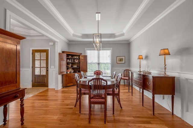 dining area with a notable chandelier, a wainscoted wall, light wood-style flooring, and a raised ceiling