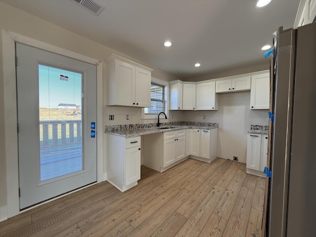 kitchen featuring sink, light wood-type flooring, white cabinetry, and light stone counters