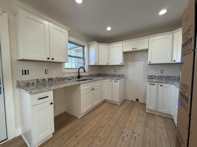 kitchen featuring white cabinetry, sink, light stone counters, and light wood-type flooring