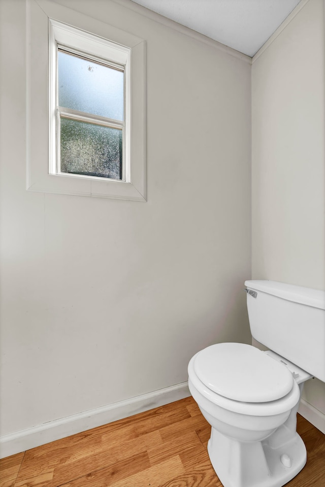 bathroom with wood-type flooring, crown molding, and toilet