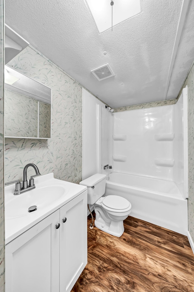 full bathroom with wood-type flooring, a textured ceiling, washtub / shower combination, vanity, and toilet