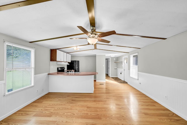 kitchen with light wood-type flooring, kitchen peninsula, ceiling fan, and black refrigerator