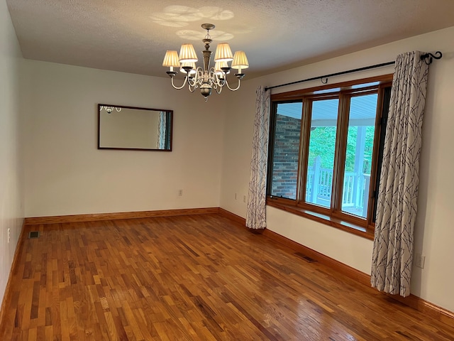 unfurnished room with a textured ceiling, an inviting chandelier, and hardwood / wood-style flooring