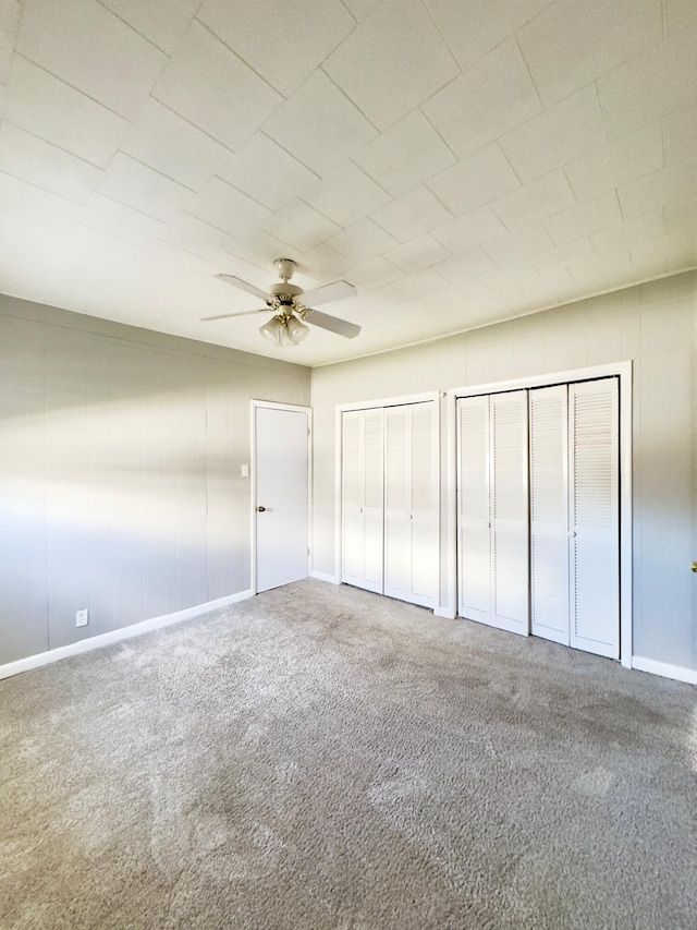 unfurnished bedroom featuring carpet flooring, ceiling fan, and two closets