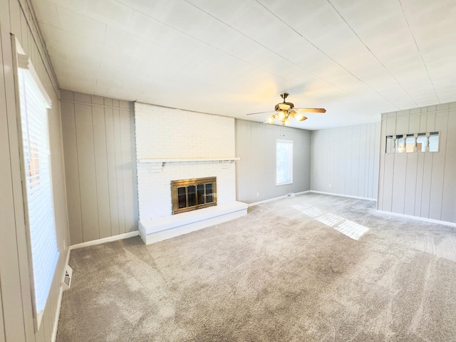 unfurnished living room featuring carpet flooring, ceiling fan, wood walls, and a brick fireplace