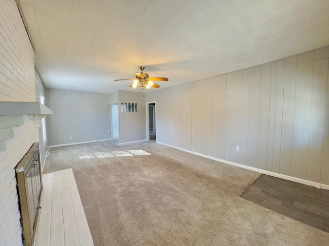 unfurnished living room featuring a fireplace, ceiling fan, wood walls, and light colored carpet