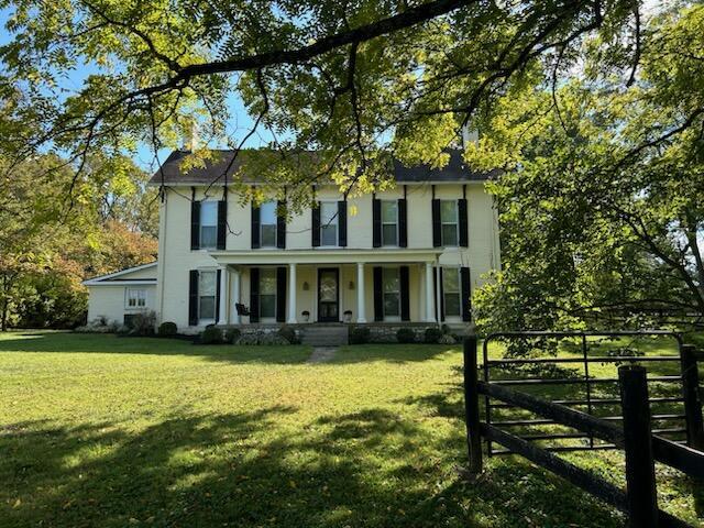 colonial house with covered porch, fence, and a front lawn