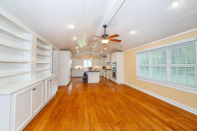 unfurnished living room with vaulted ceiling, built in features, a wealth of natural light, and light hardwood / wood-style flooring