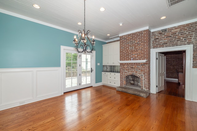 unfurnished living room with french doors, light hardwood / wood-style floors, a notable chandelier, a brick fireplace, and crown molding