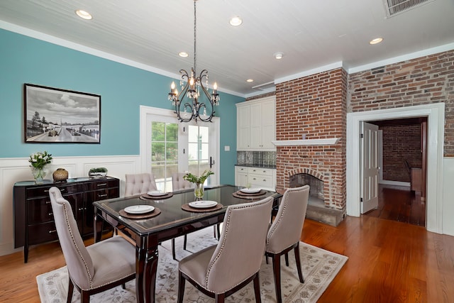 dining room featuring brick wall, a fireplace, light hardwood / wood-style floors, ornamental molding, and a chandelier