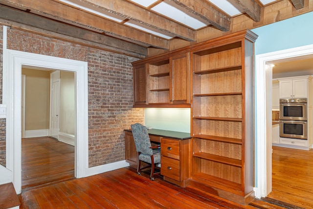 unfurnished office with brick wall, dark hardwood / wood-style flooring, and beam ceiling