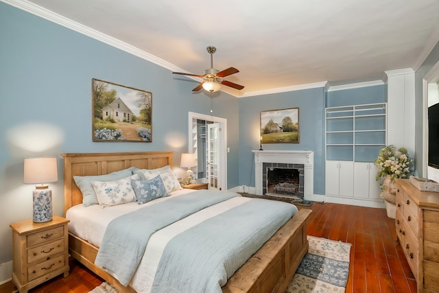 bedroom with ceiling fan, a tiled fireplace, dark hardwood / wood-style floors, and crown molding