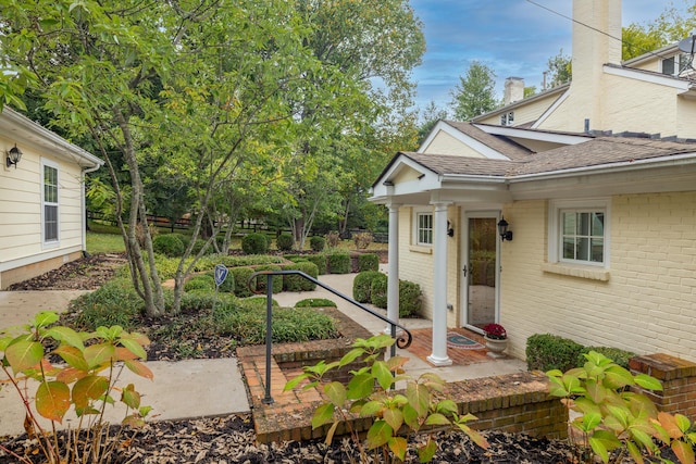 doorway to property featuring brick siding, fence, and a shingled roof