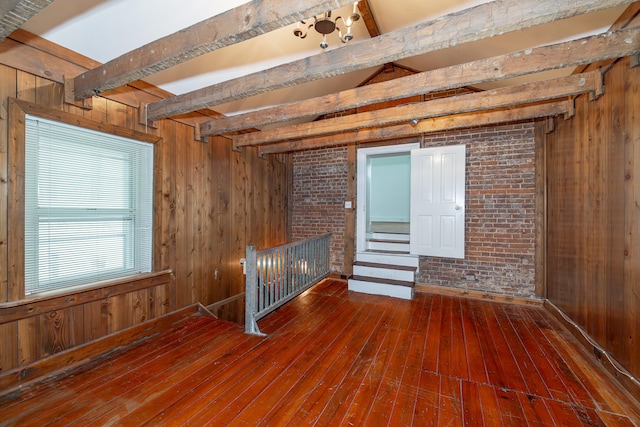 unfurnished room with brick wall, dark wood-type flooring, beamed ceiling, and wood walls