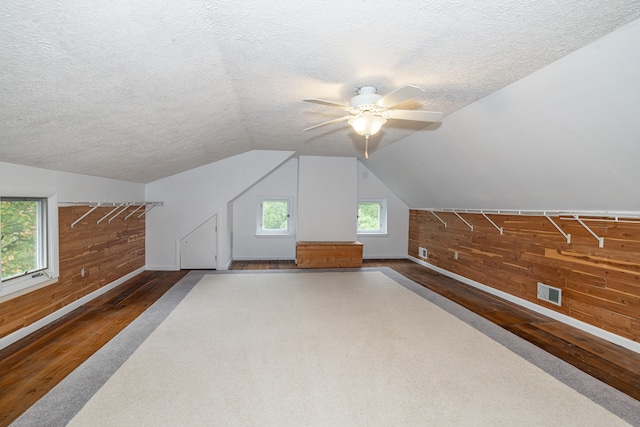 additional living space with vaulted ceiling, ceiling fan, a textured ceiling, and wood walls