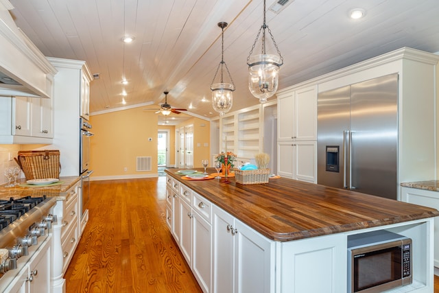 kitchen featuring appliances with stainless steel finishes, butcher block counters, decorative light fixtures, and a center island