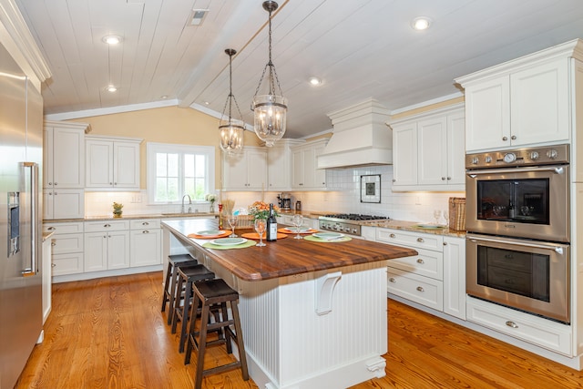 kitchen with white cabinets, a center island, lofted ceiling, wooden counters, and stainless steel appliances