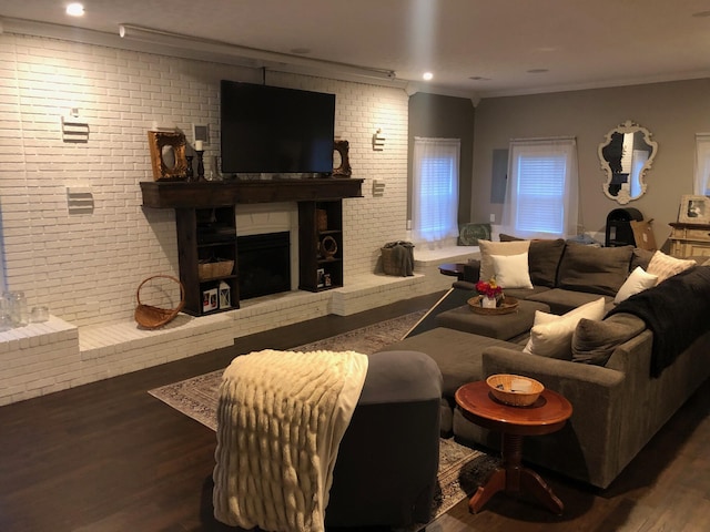 living room with brick wall, wood finished floors, crown molding, a brick fireplace, and recessed lighting