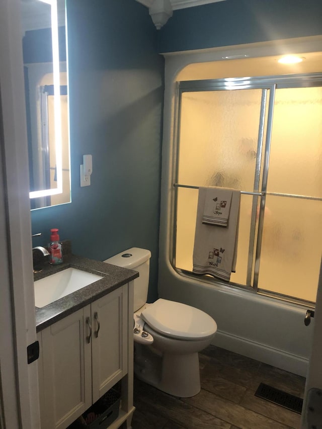 bathroom with toilet, bath / shower combo with glass door, wood finished floors, vanity, and visible vents