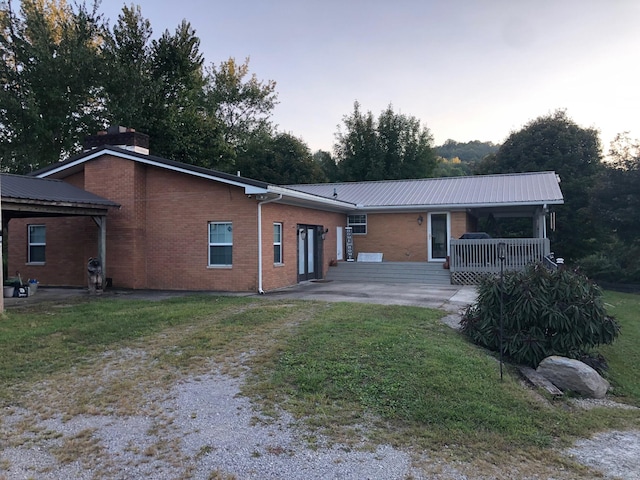 rear view of property featuring a yard, metal roof, brick siding, and driveway