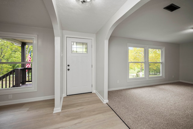 foyer entrance with a wealth of natural light, a textured ceiling, and light wood-type flooring