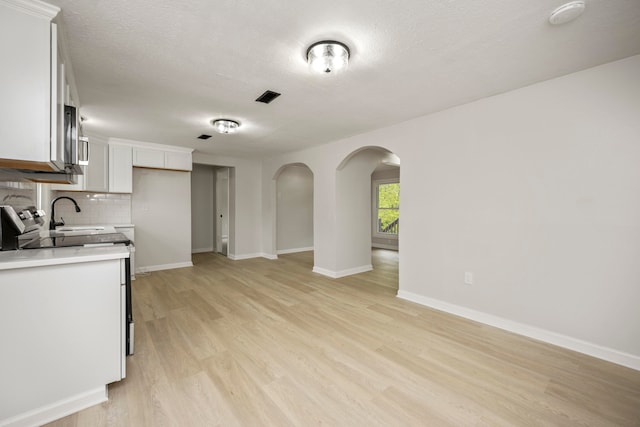 kitchen with electric range, backsplash, white cabinetry, a textured ceiling, and light hardwood / wood-style floors