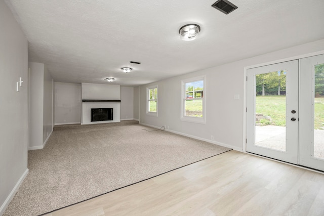 unfurnished living room featuring french doors, light hardwood / wood-style floors, and a textured ceiling