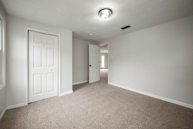 unfurnished bedroom featuring a textured ceiling, carpet floors, and a closet