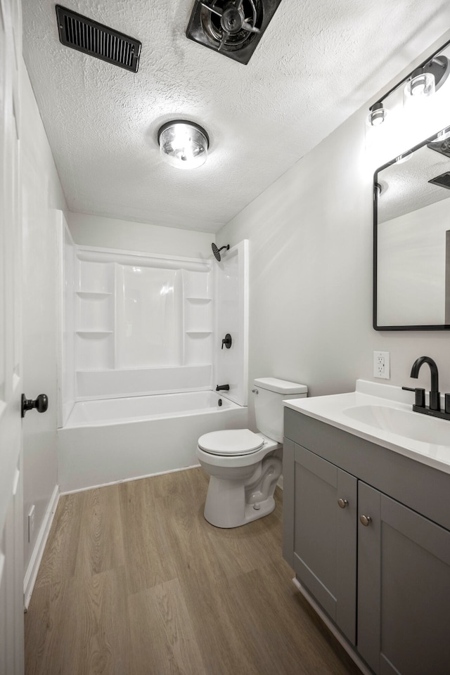 full bathroom with a textured ceiling, hardwood / wood-style flooring, toilet, vanity, and washtub / shower combination