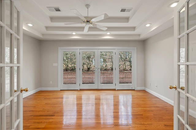 unfurnished room with light hardwood / wood-style floors, ceiling fan, a tray ceiling, and french doors