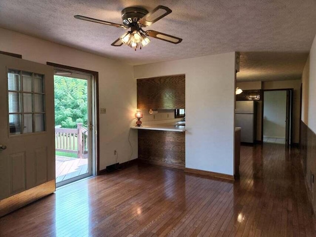 unfurnished living room featuring ceiling fan, dark wood-type flooring, and a textured ceiling