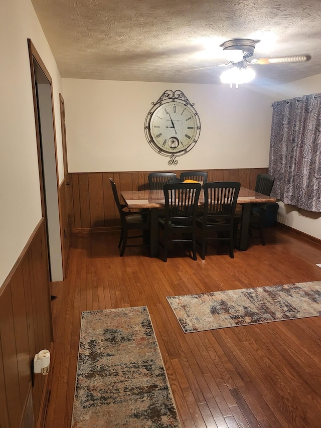 dining space featuring a textured ceiling, wood-type flooring, wood walls, and ceiling fan