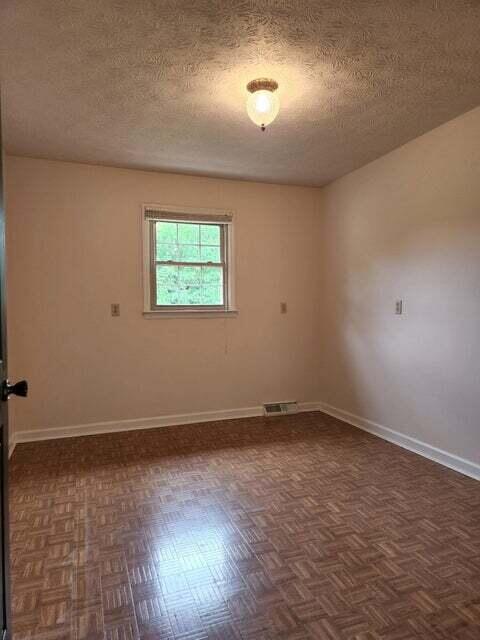 spare room with a textured ceiling and dark parquet flooring