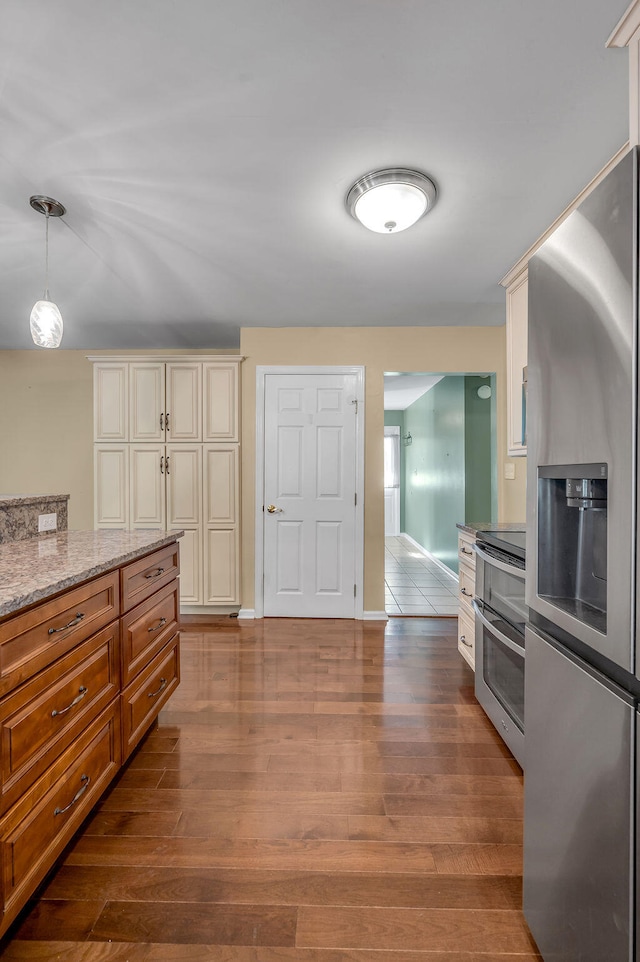 kitchen featuring pendant lighting, hardwood / wood-style flooring, cream cabinetry, stainless steel appliances, and light stone countertops