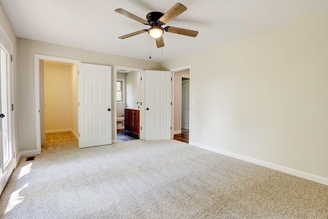 unfurnished bedroom with carpet flooring, ensuite bath, multiple windows, and ceiling fan