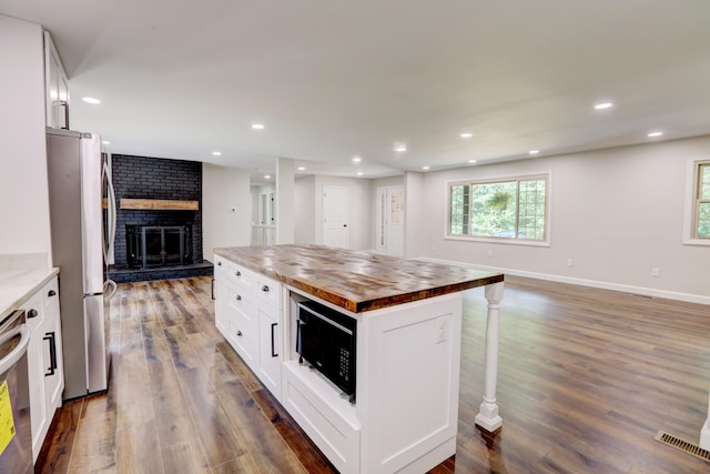 kitchen with wood counters, dark wood-type flooring, white cabinetry, a kitchen island, and stainless steel appliances