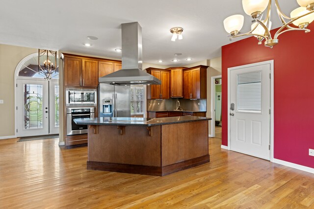 kitchen with a notable chandelier, stainless steel appliances, island range hood, and decorative light fixtures