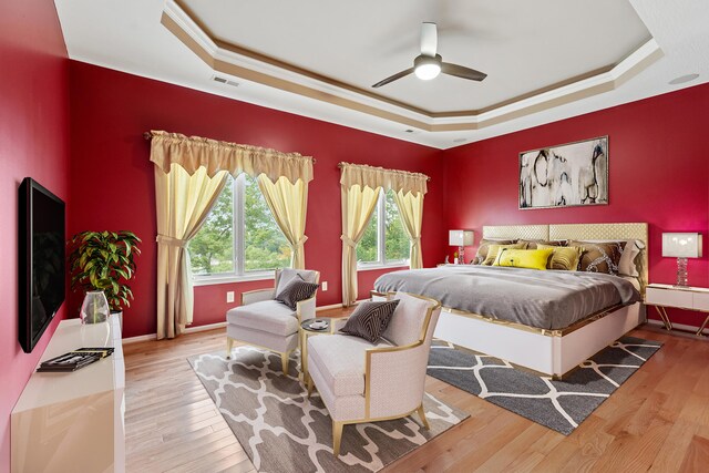 bedroom featuring ornamental molding, a tray ceiling, light hardwood / wood-style floors, and ceiling fan