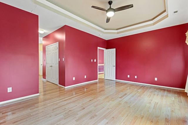 spare room featuring light hardwood / wood-style floors, ceiling fan, a tray ceiling, and crown molding