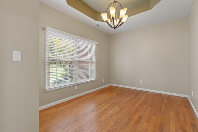 empty room with an inviting chandelier, a tray ceiling, and hardwood / wood-style flooring