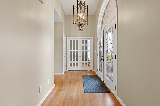 interior space with light wood-type flooring, a chandelier, a high ceiling, and french doors