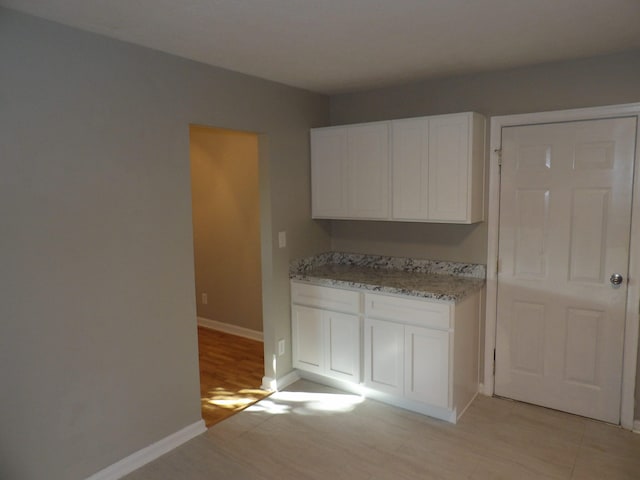 kitchen featuring light wood-type flooring, white cabinetry, and light stone counters