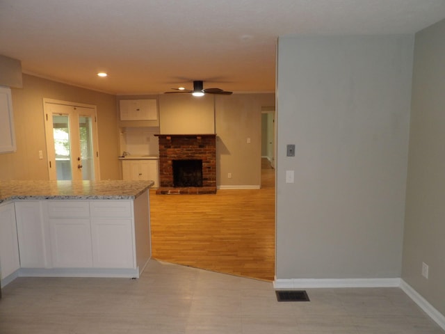 kitchen with light stone counters, light hardwood / wood-style floors, white cabinetry, a brick fireplace, and ceiling fan