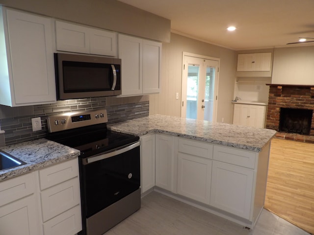 kitchen featuring light wood-type flooring, white cabinetry, kitchen peninsula, a fireplace, and stainless steel appliances