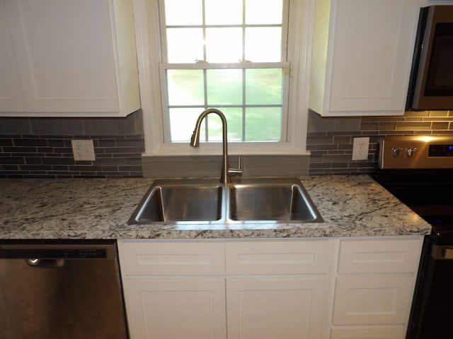 kitchen featuring appliances with stainless steel finishes, decorative backsplash, white cabinets, light stone countertops, and sink