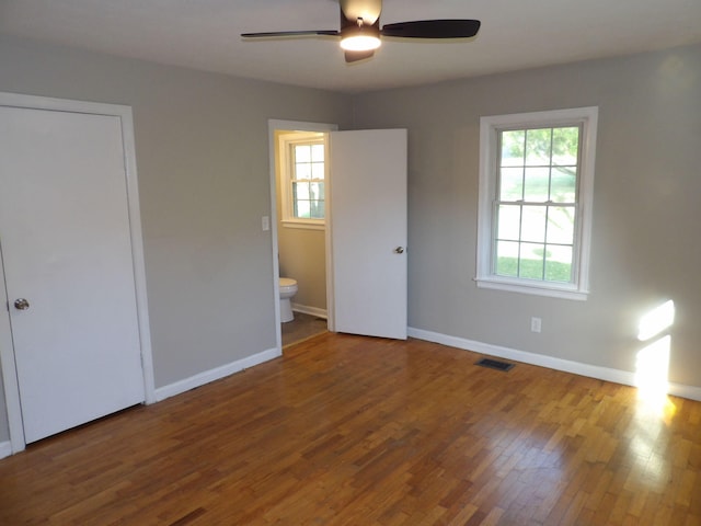 unfurnished bedroom featuring wood-type flooring, a closet, connected bathroom, and ceiling fan