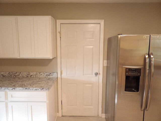 kitchen with light tile patterned flooring, light stone countertops, stainless steel fridge, and white cabinetry